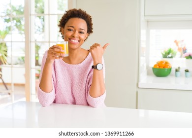 Young african american woman driking orange juice at home pointing and showing with thumb up to the side with happy face smiling - Shutterstock ID 1369911266