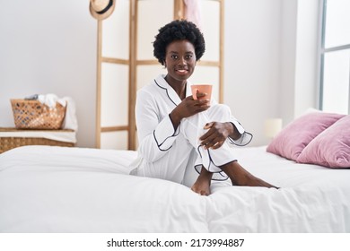Young african american woman drinking cup of coffee sitting on bed at bedroom