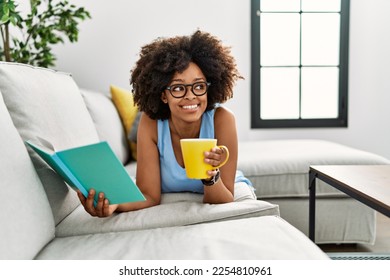 Young african american woman drinking coffee reading book at home - Powered by Shutterstock