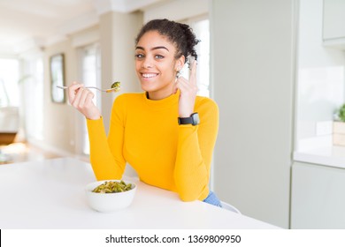 Young african american woman eating healthy green vegatables surprised with an idea or question pointing finger with happy face, number one - Shutterstock ID 1369809950