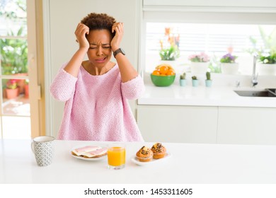 Young african american woman eating breaksfast in the morning at home suffering from headache desperate and stressed because pain and migraine. Hands on head.