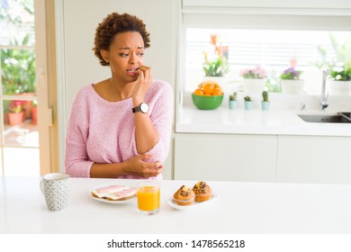 Young african american woman eating breaksfast in the morning at home looking stressed and nervous with hands on mouth biting nails. Anxiety problem.