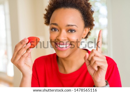 Young african american woman eating fresh strawberries for breakfast surprised with an idea or question pointing finger with happy face, number one