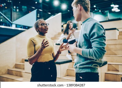 Young African American Woman Explaining Information To Male Colleague Standing On Break In Coworking Office, Multiracial Students In Casual Wear Communicating On Free Time Share Ideas For Project
