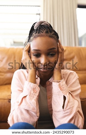 A young African American woman feeling sad, resting her face in her hands. She's seated indoors, her expression conveying a sense of contemplation or concern.