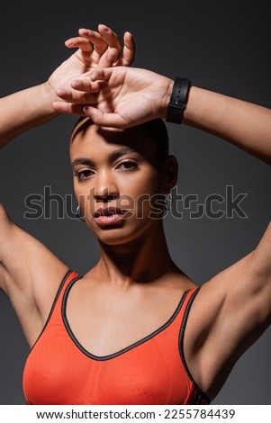 young african american woman with fitness tracker posing with raised hands isolated on grey