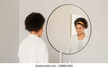 Young African American Woman Getting Dressed Looking In Mirror. Trying On White Shirt Clothes Enjoying Preens Herself, Admires And Straightening And Getting Ready For Date. 