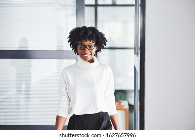 Young African American Woman In Glasses Stands Indoors In The Office.