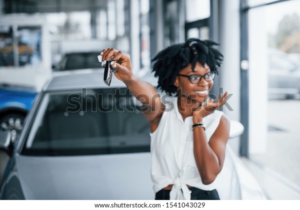 Young african american woman in glasses stands\
indoors with keys in\
hands.