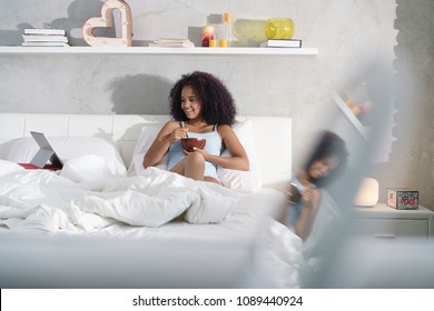 Young African American Woman Having Breakfast In Bed At Home. Portrait Of Happy Black Girl Smiling While Watching Movie On Computer TV On Weekend.