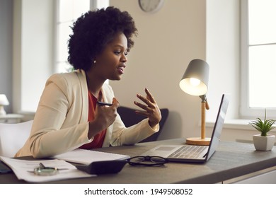 Young African American Woman Having Conference Video Call Using Laptop Talking To Coworker Online Audience Sitting At Office Desk In Evening. Consultation, Webinar, Tutoring On Internet, Telecommuting