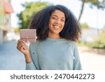 Young African American woman holding a wallet at outdoors smiling a lot