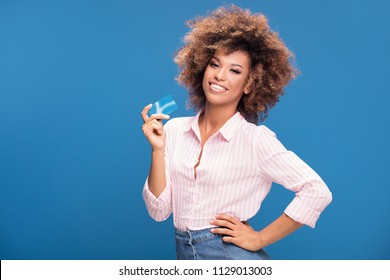 Young African American Woman Holding Credit Card In Hand, Smiling To The Camera, Posing On Blue Studio Background.