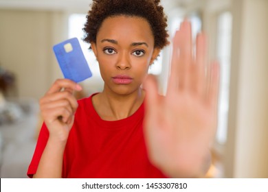 Young african american woman holding credit card with open hand doing stop sign with serious and confident expression, defense gesture Stock fotografie