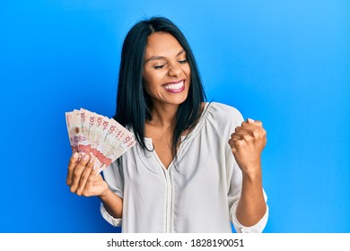 Young african american woman holding 10 colombian pesos banknotes very happy and excited doing winner gesture with arms raised, smiling and screaming for success. celebration concept. 