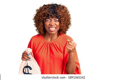 Young African American Woman Holding Money Bag With Dollar Symbol Annoyed And Frustrated Shouting With Anger, Yelling Crazy With Anger And Hand Raised 