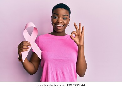 Young African American Woman Holding Pink Cancer Ribbon Doing Ok Sign With Fingers, Smiling Friendly Gesturing Excellent Symbol 