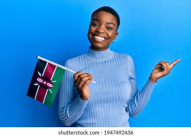 Young african american woman holding kenya flag smiling happy pointing with hand and finger to the side 