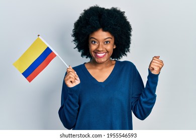 Young african american woman holding colombia flag screaming proud, celebrating victory and success very excited with raised arm 