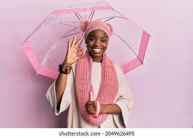 Young african american woman holding umbrella doing ok sign with fingers, smiling friendly gesturing excellent symbol 