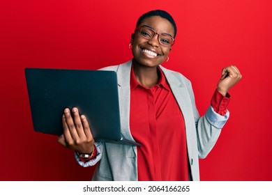 Junge afrikanische Amerikanerin, die einen Laptop hält, stolz schreiend, feierlich Sieg und Erfolg sehr aufgeregt mit erhabenem Arm 