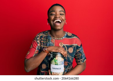 Young African American Woman Holding Savings Jar With South African Rands Money Smiling And Laughing Hard Out Loud Because Funny Crazy Joke. 