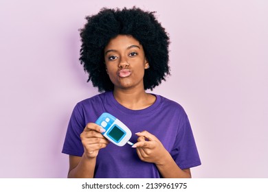 Young african american woman holding glucometer device looking at the camera blowing a kiss being lovely and sexy. love expression. 