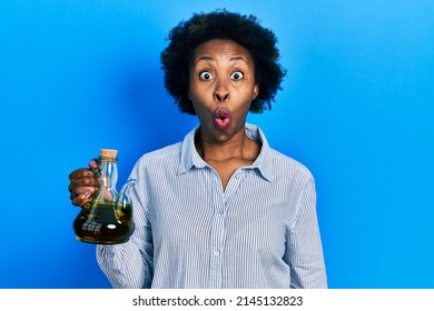 Young african american woman holding olive oil can scared and amazed with open mouth for surprise, disbelief face 