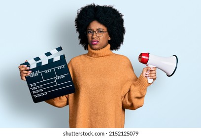 Young African American Woman Holding Video Film Clapboard And Megaphone Clueless And Confused Expression. Doubt Concept. 