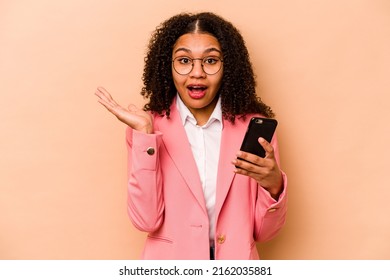 Young African American Woman Holding Mobile Phone Isolated On Beige Background Surprised And Shocked.