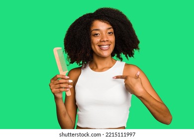 Young African American Woman Holding Hair Comb Isolated Person Pointing By Hand To A Shirt Copy Space, Proud And Confident