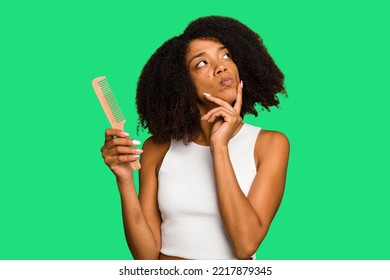 Young African American Woman Holding Hair Comb Isolated Looking Sideways With Doubtful And Skeptical Expression.