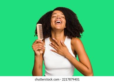 Young African American Woman Holding Hair Comb Isolated Laughs Out Loudly Keeping Hand On Chest.