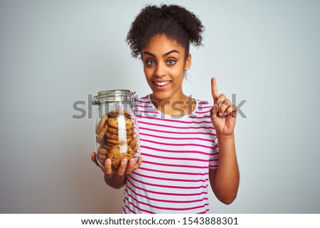 Young african american woman holding a jar of cookies over isolated white background surprised with an idea or question pointing finger with happy face, number one