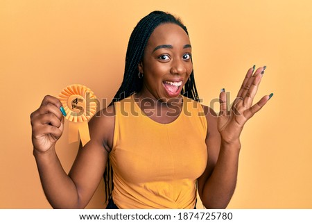 Young african american woman holding fourth place badge celebrating victory with happy smile and winner expression with raised hands 
