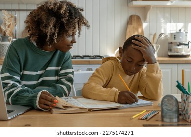 Young African American woman homeschool mom helping son with homework, mother and child studying at home together. Parent sitting at table with kid checking assignment. Parenthood and homeschooling - Powered by Shutterstock