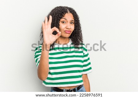 Young african american woman isolated on white background winks an eye and holds an okay gesture with hand.