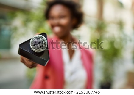 Young african american woman journalist pointing reporter microphone to the camera for television news