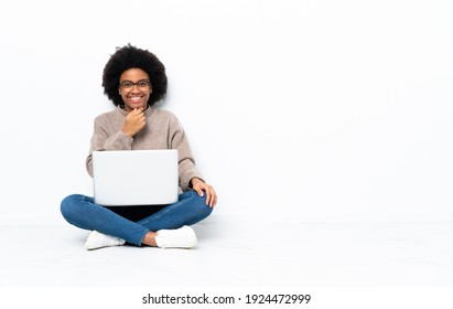 Junge Afroamerikanerin mit einem Laptop auf dem Boden mit Gläsern und Lächeln