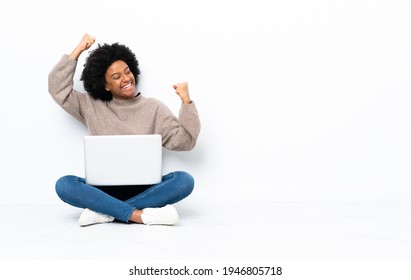 Young African American Woman With A Laptop Sitting On The Floor Celebrating A Victory