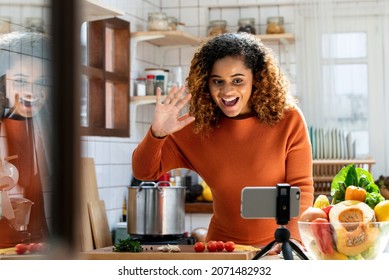 Young African American Woman Looking At Mobile Phone And Say Hi On Social Media In Kitchen At Home, Virtual Cooking Class Concept