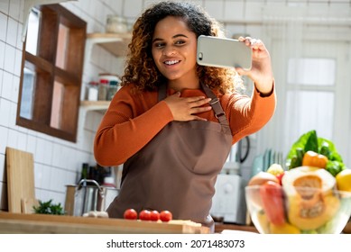 Young African American Woman Looking At Mobile Phone Making Video Call While Cooking In Kitchen At Home