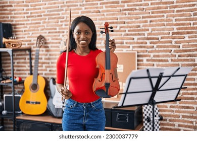 Young african american woman musician holding violin at music studio - Powered by Shutterstock