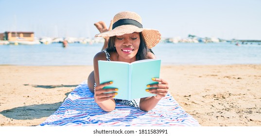 Young African American Woman On Vacation Laying On The Towel Reading Book At The Beach