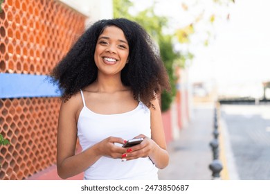 Young African American woman at outdoors sending a message with the mobile - Powered by Shutterstock