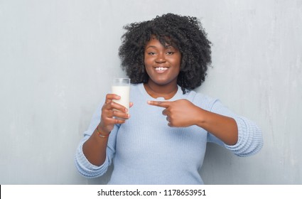 Young african american woman over grey grunge wall drinking a glass of milk very happy pointing with hand and finger