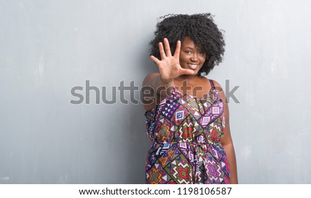 Young african american woman over grey grunge wall wearing colorful dress showing and pointing up with fingers number five while smiling confident and happy.