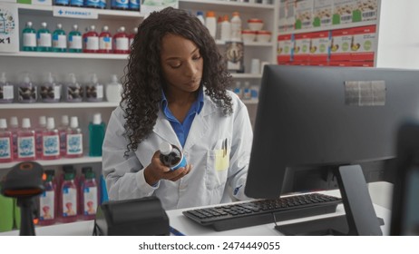 A young african american woman pharmacist with curly hair examines a bottle in a well-organized pharmacy, surrounded by shelves of medical supplies and using a computer. - Powered by Shutterstock