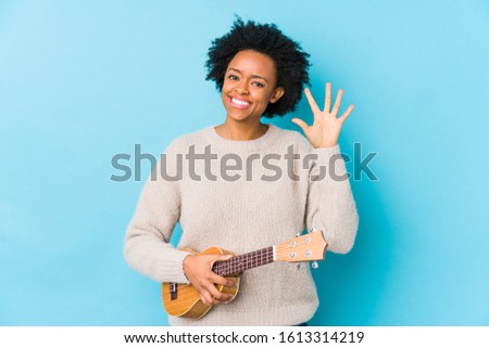 Young african american woman playing ukelele isolated smiling cheerful showing number five with fingers.