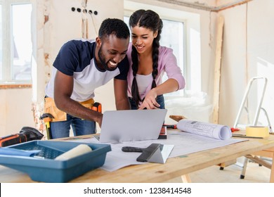 Young African American Woman Pointing At Laptop Screen To Boyfriend During Renovation Of Home